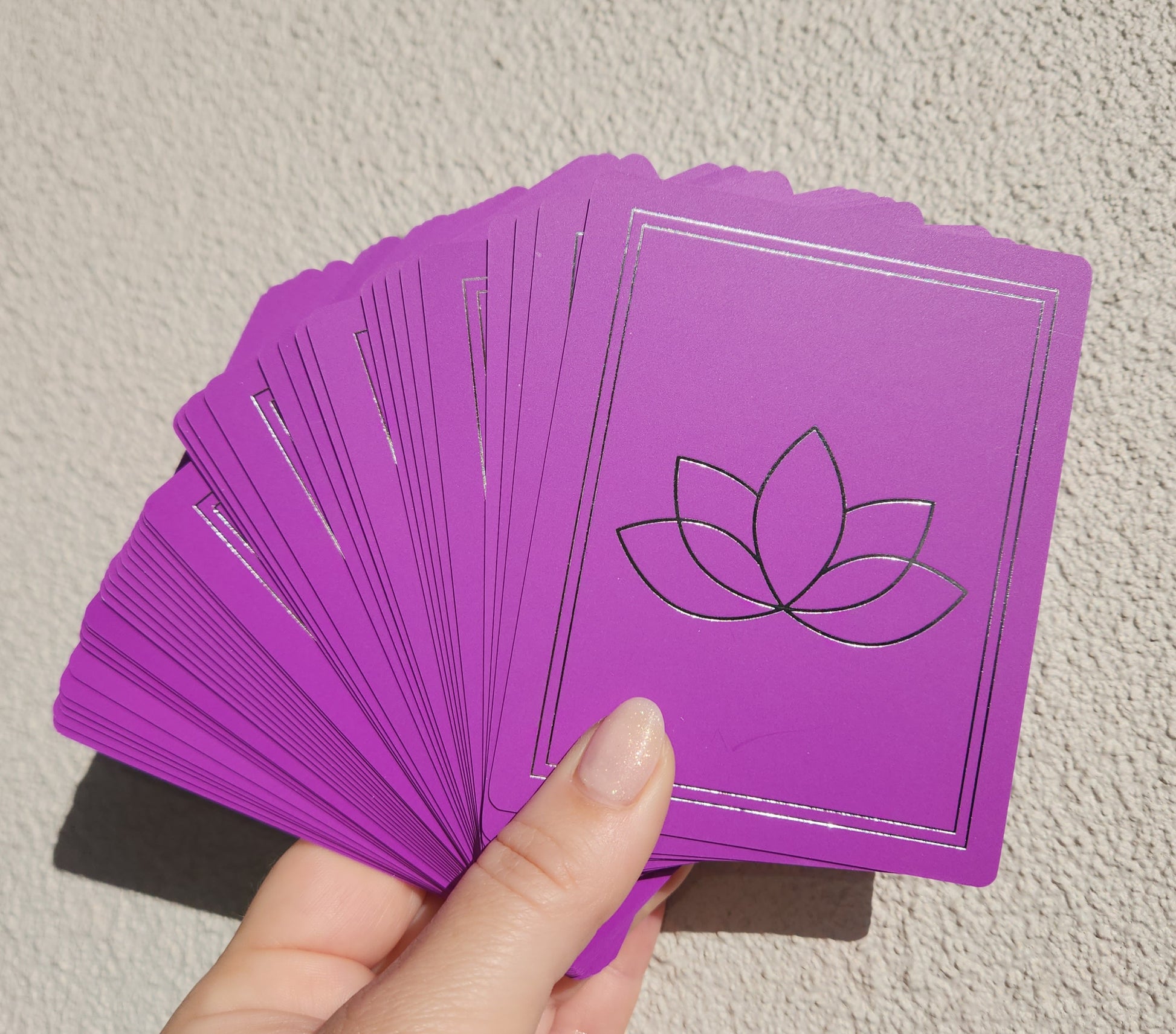 Purple cards with a lotus symbol held by a hand against a neutral background