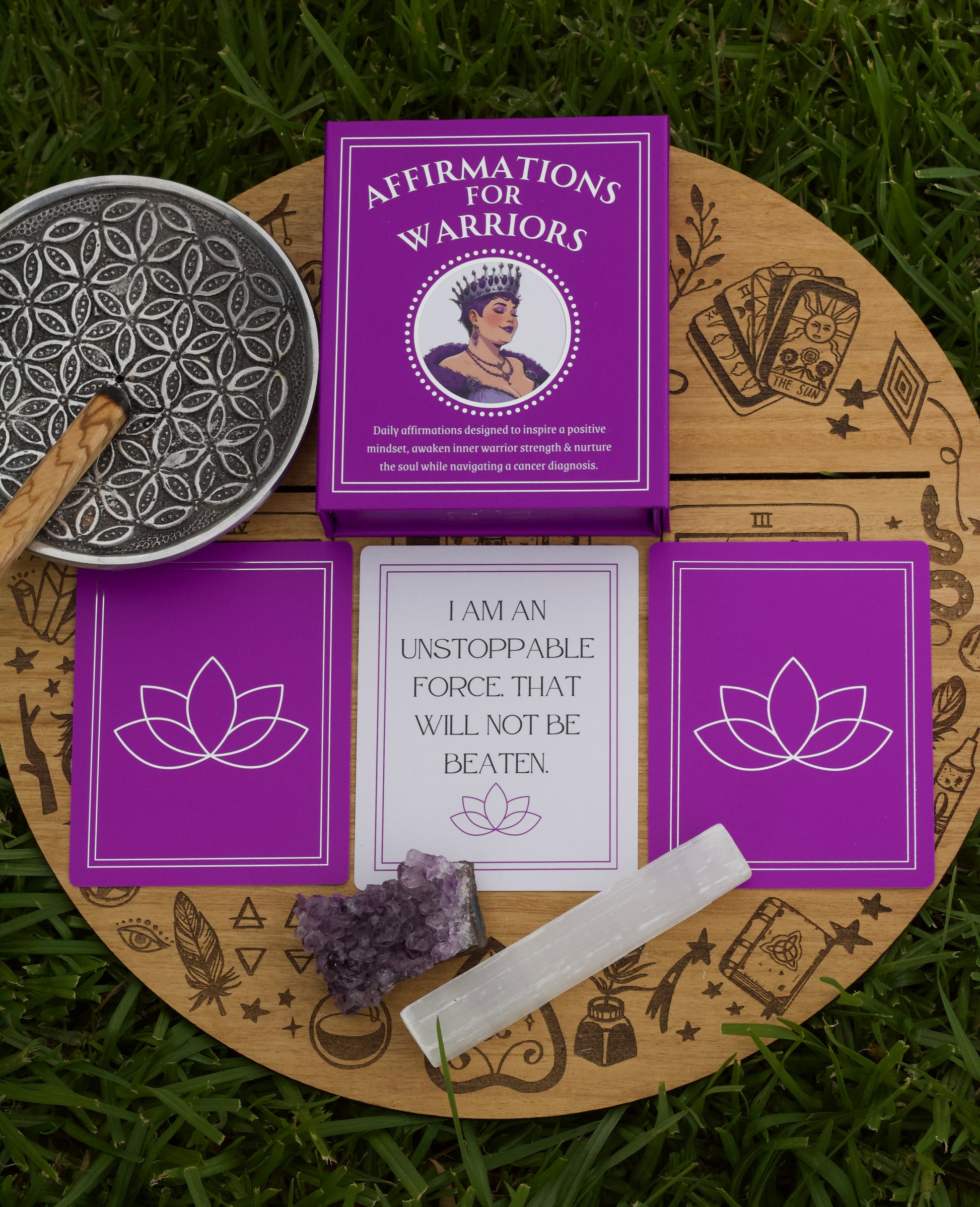 Purple affirmation cards titled 'Affirmations for Warriors' on a wooden board with amethyst crystal and other items on grass.